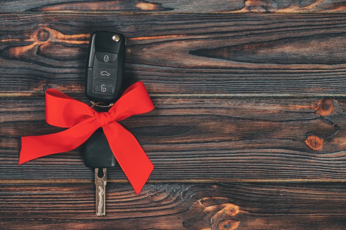 Car key with a red bow attached, placed on a dark wooden surface.